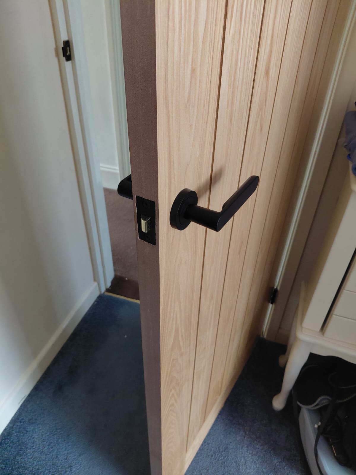 Close-up of oak door with black lever handle and latch