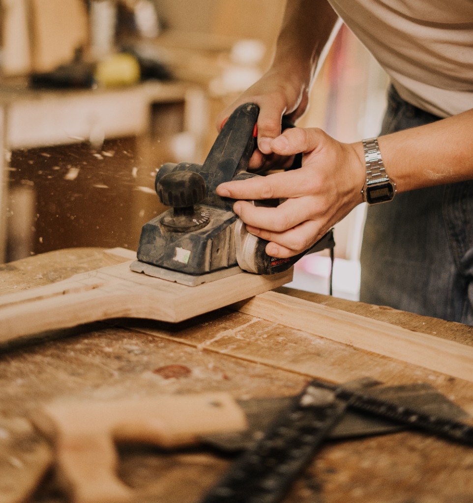Carpenter planing timber on a workbench, sawdust in the air