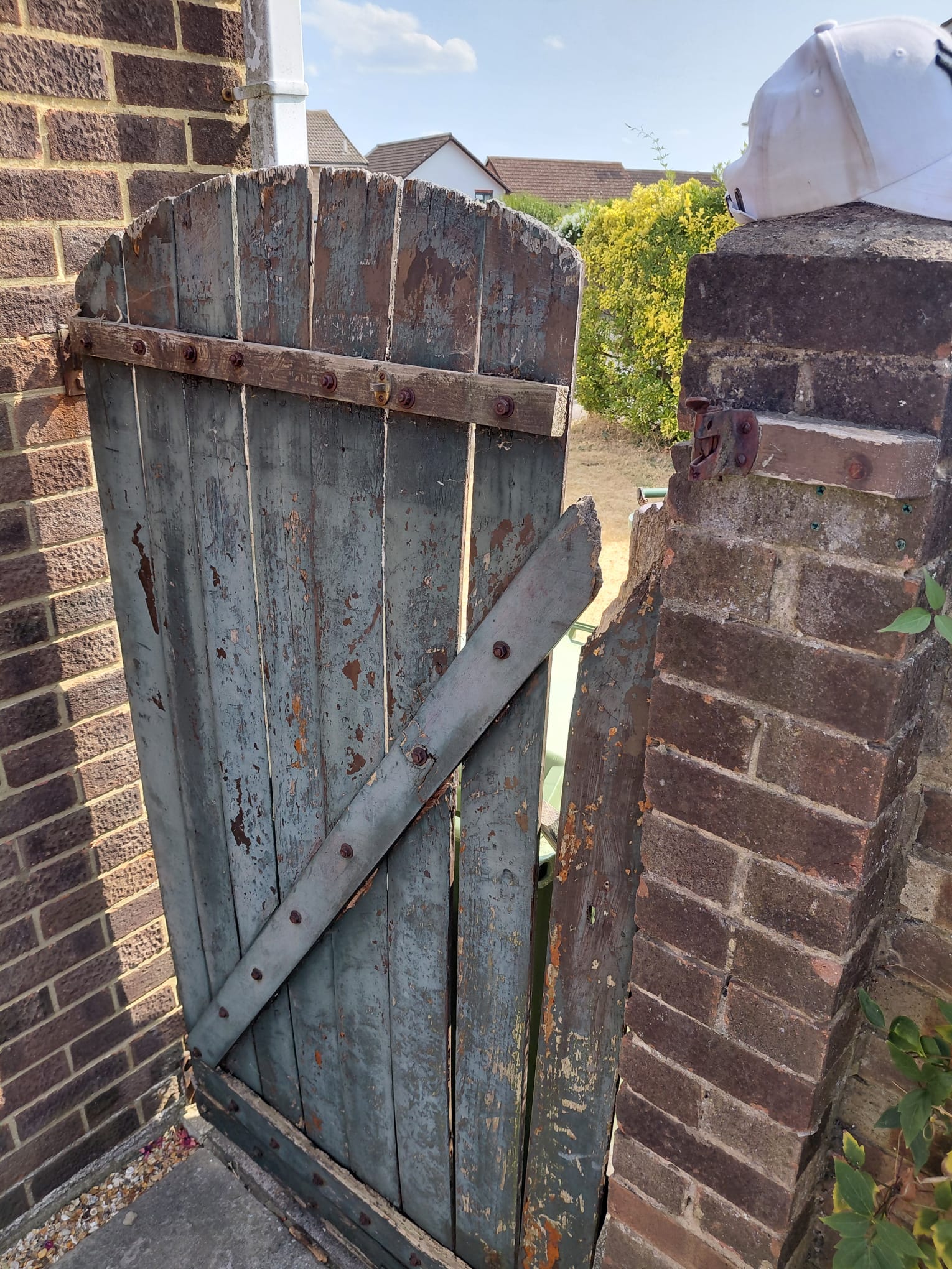 Old painted side gate with rotten boards and a missing board on the latch side